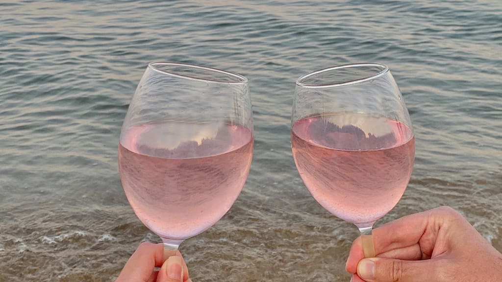 holding two glasses of rose in front of the sea